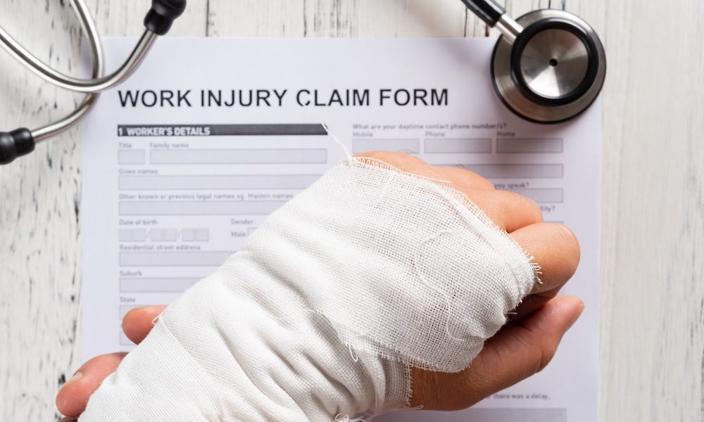 New Year, Same PBA Workers’ Compensation Program: Your Trusted Solution - Person holding a bandaged arm in front of a work injury claim form